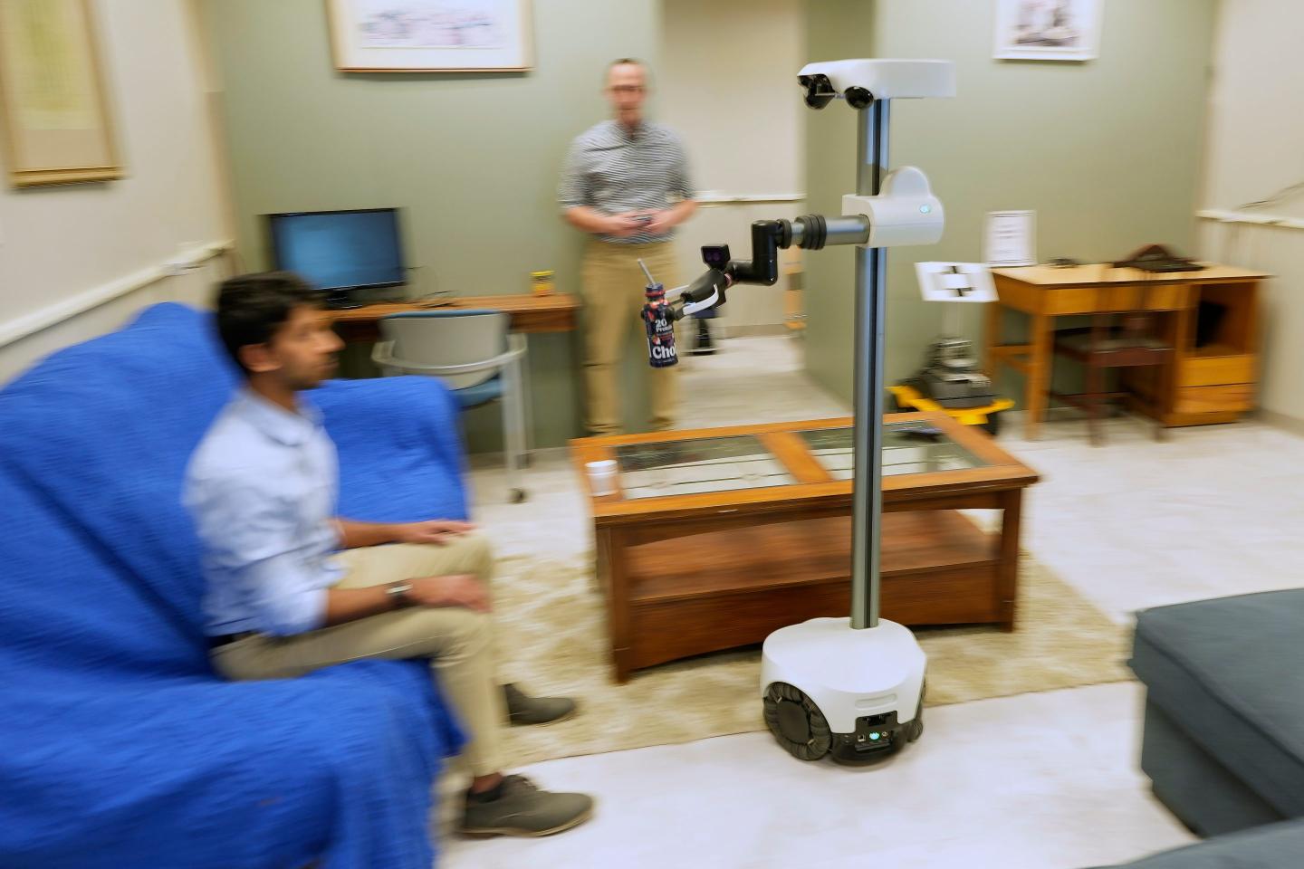 A robot operated by a robotics engineer, rear, brings a drink to colleague during a demonstration at the University of New Hampshire, Tuesday, April 21, 2026, in Durham, N.H.