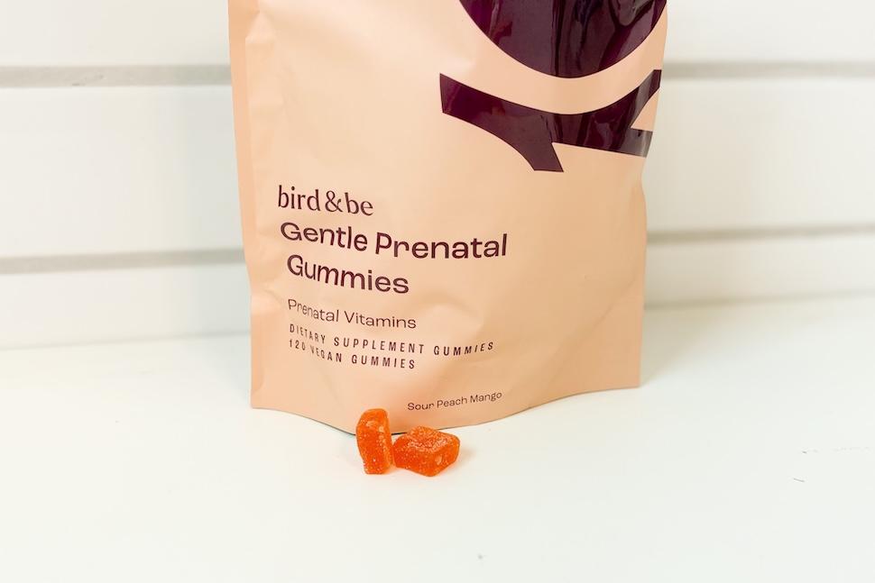 A tan bag of Bird&Be Gentle Prenatal Gummies sitting on a white countertop. Two of the orange gummies are next to the bag.