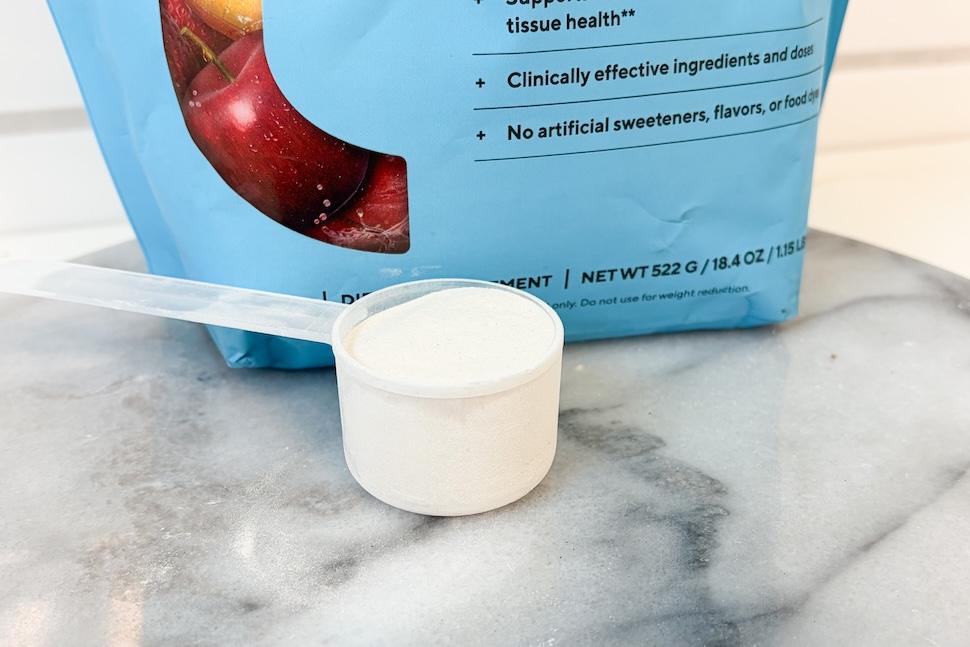 Closeup of a bag of Legion Collagen+ sitting on a marble tabletop. A plastic scooper sitting next to it has been packed with white power.