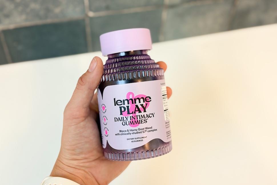 A hand holding a purple bottle of Lemme Play gummies