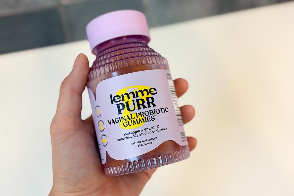 Closeup of a hand holding a purple bottle of Lemme Purr gummies