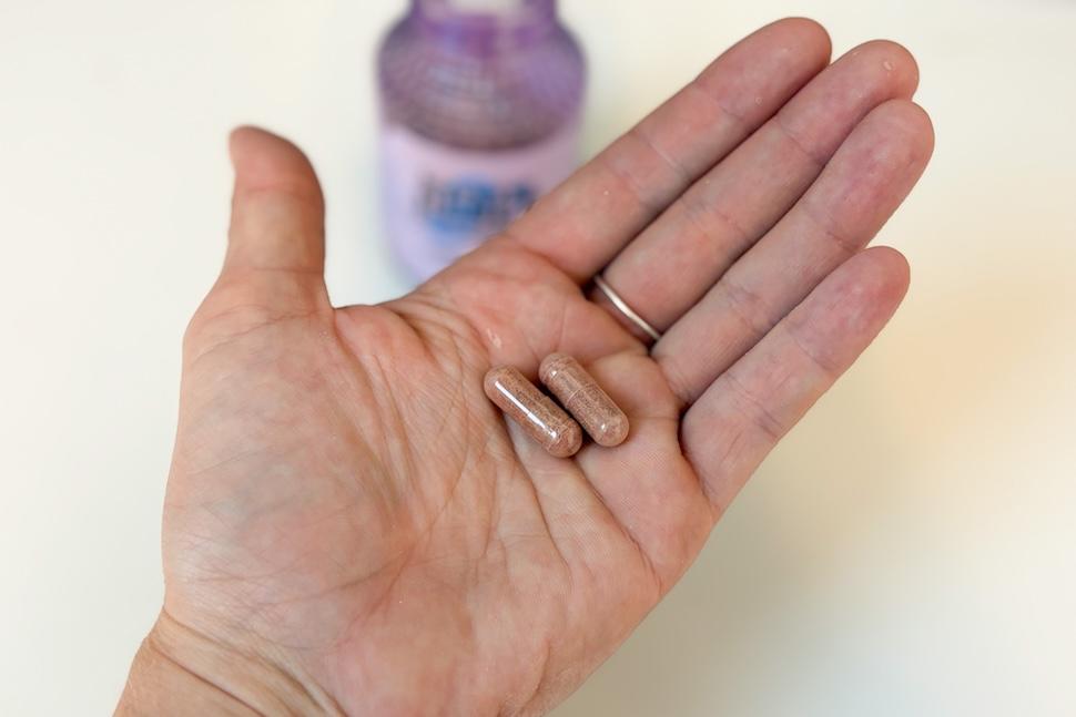 A closeup shot of an open palm holding two Lemme Reset capsules. On the countertop below, you can see the lavender bottle in the background.