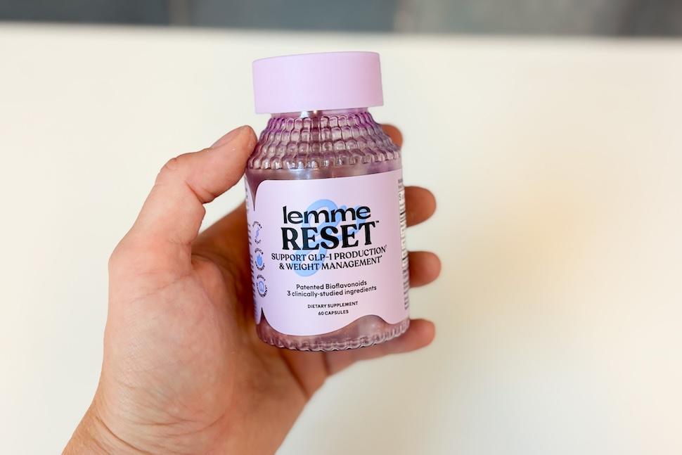 A hand holding a lavender-colored bottle of Lemme Reset pills
