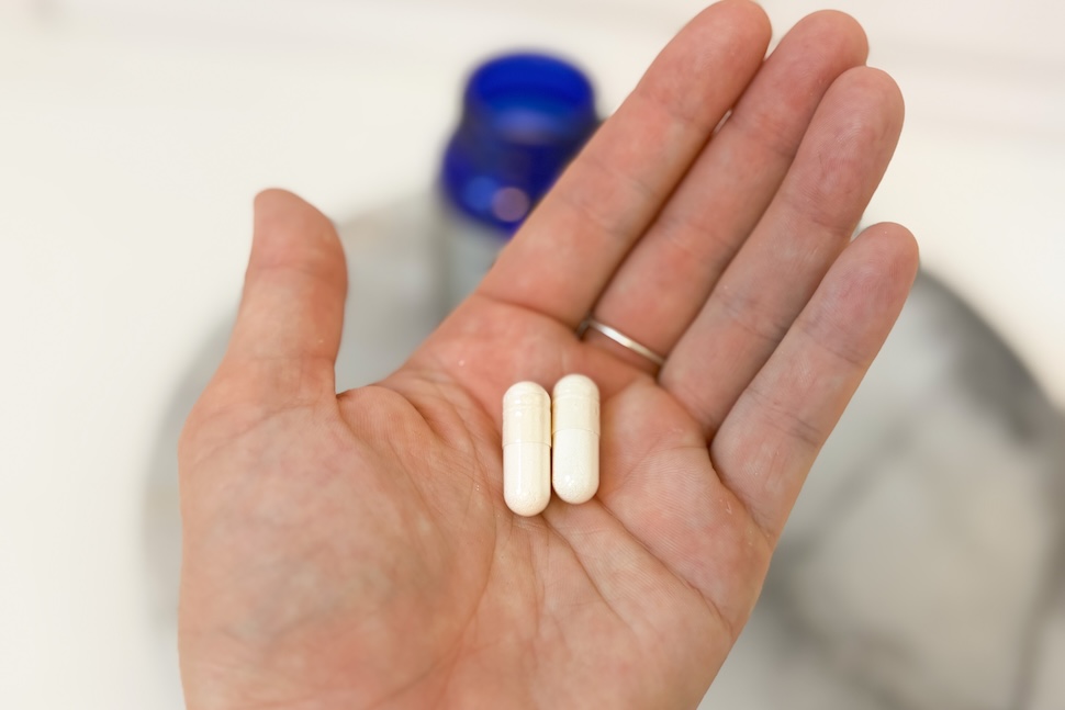 Closeup of a hand holding two off-white capsules of Tru Niagen 1,000