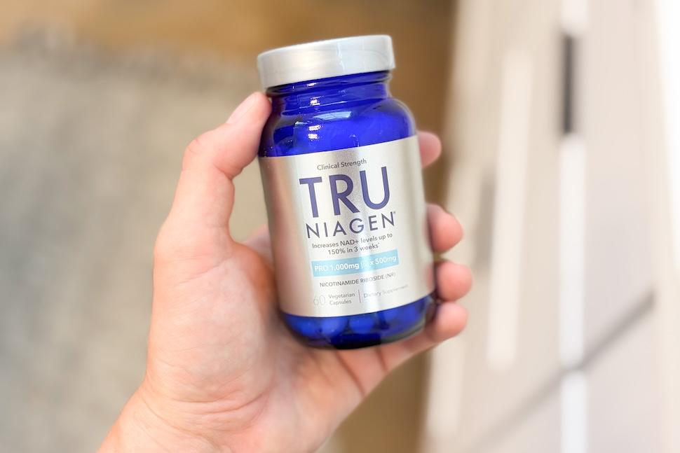 Closeup shot of a hand holding a blue bottle of Tru Niagen 1,000 mg