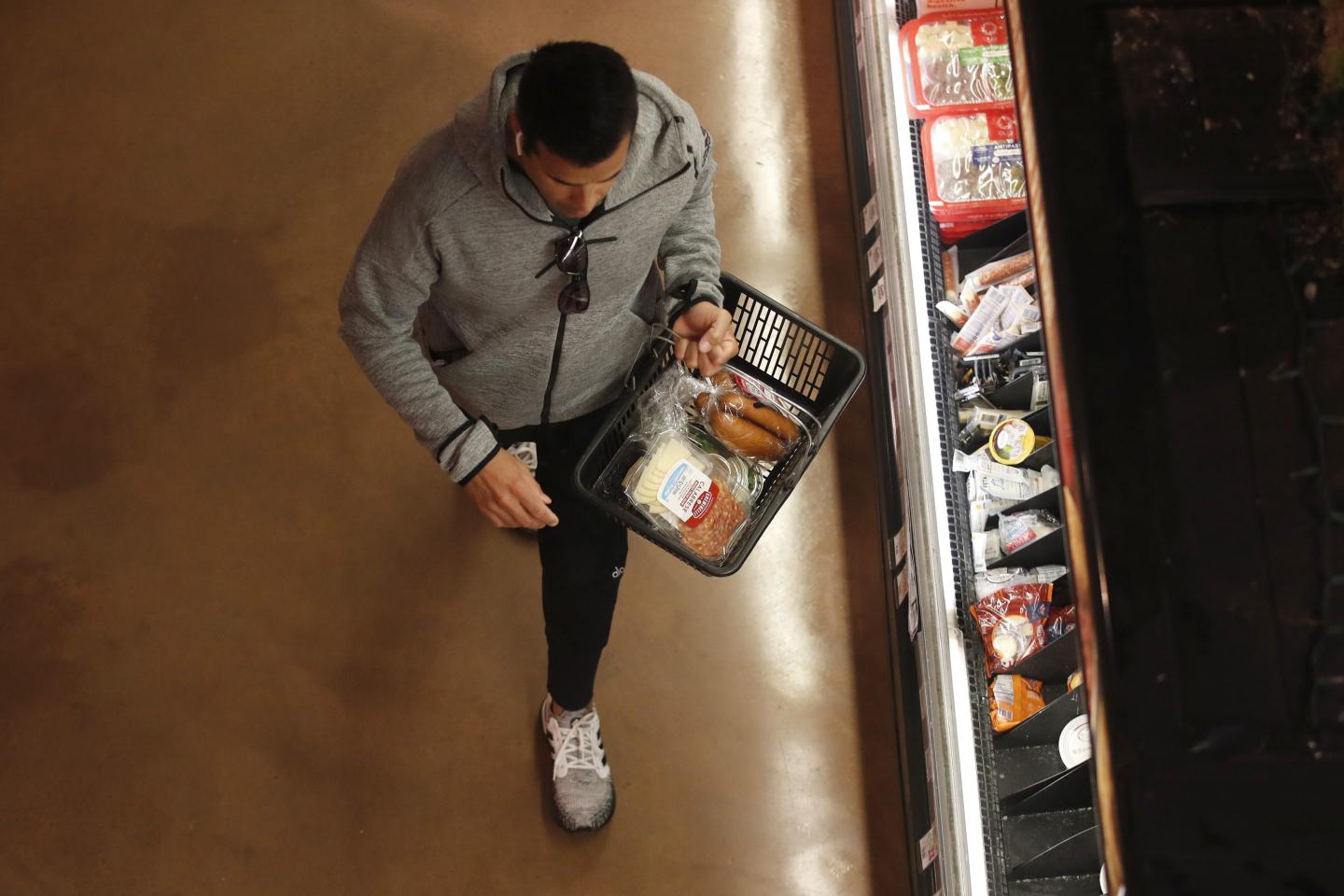 A man holds a grocery basket and walks down the aisle of a store.