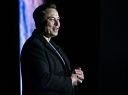 Elon Musk, wearing all black, smiles and looks to the side.