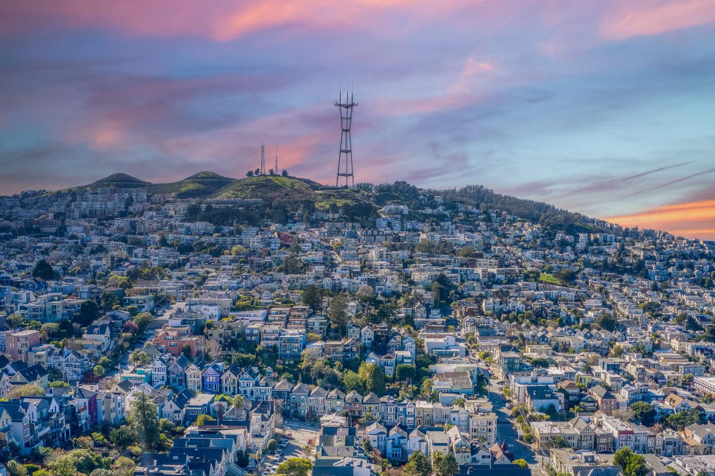 Pastel colored sky casting shadows over the colorful houses and behind Sutro Tower.