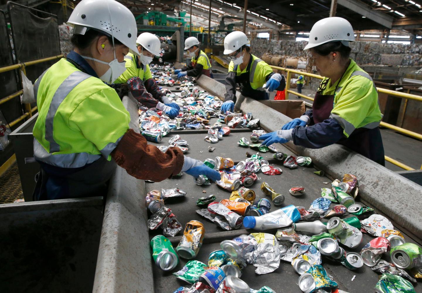 A team of workers sort aluminum cans near large bales of plastics
