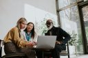 Three coworkers sit around a computer.