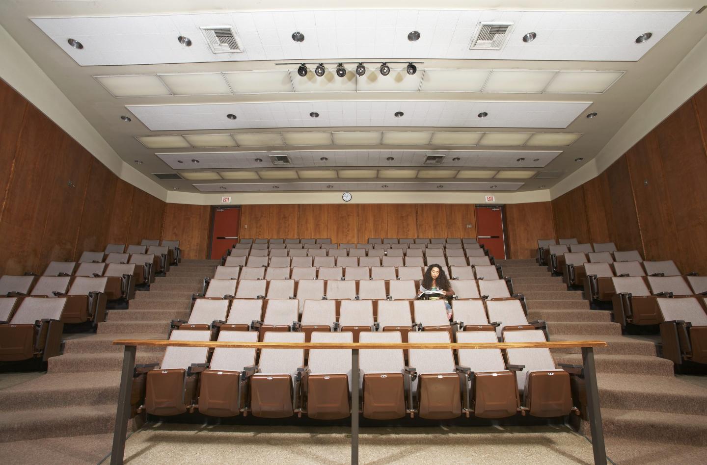 Female student reading in empty classroom auditorium, low angle view