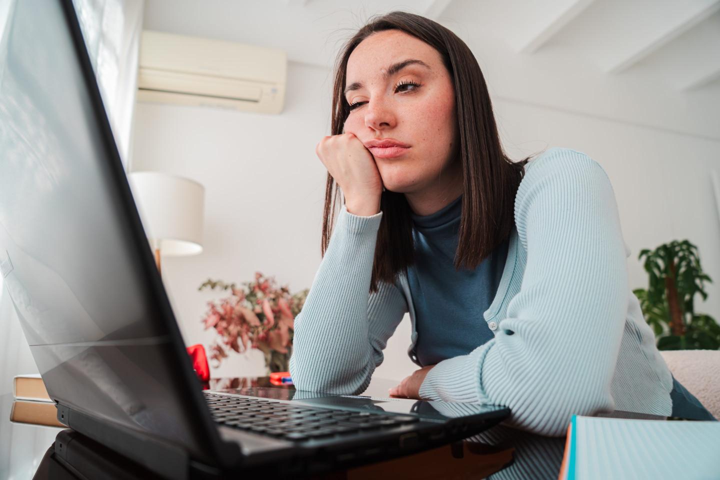 young woman looking frustrated while working on her laptop at home