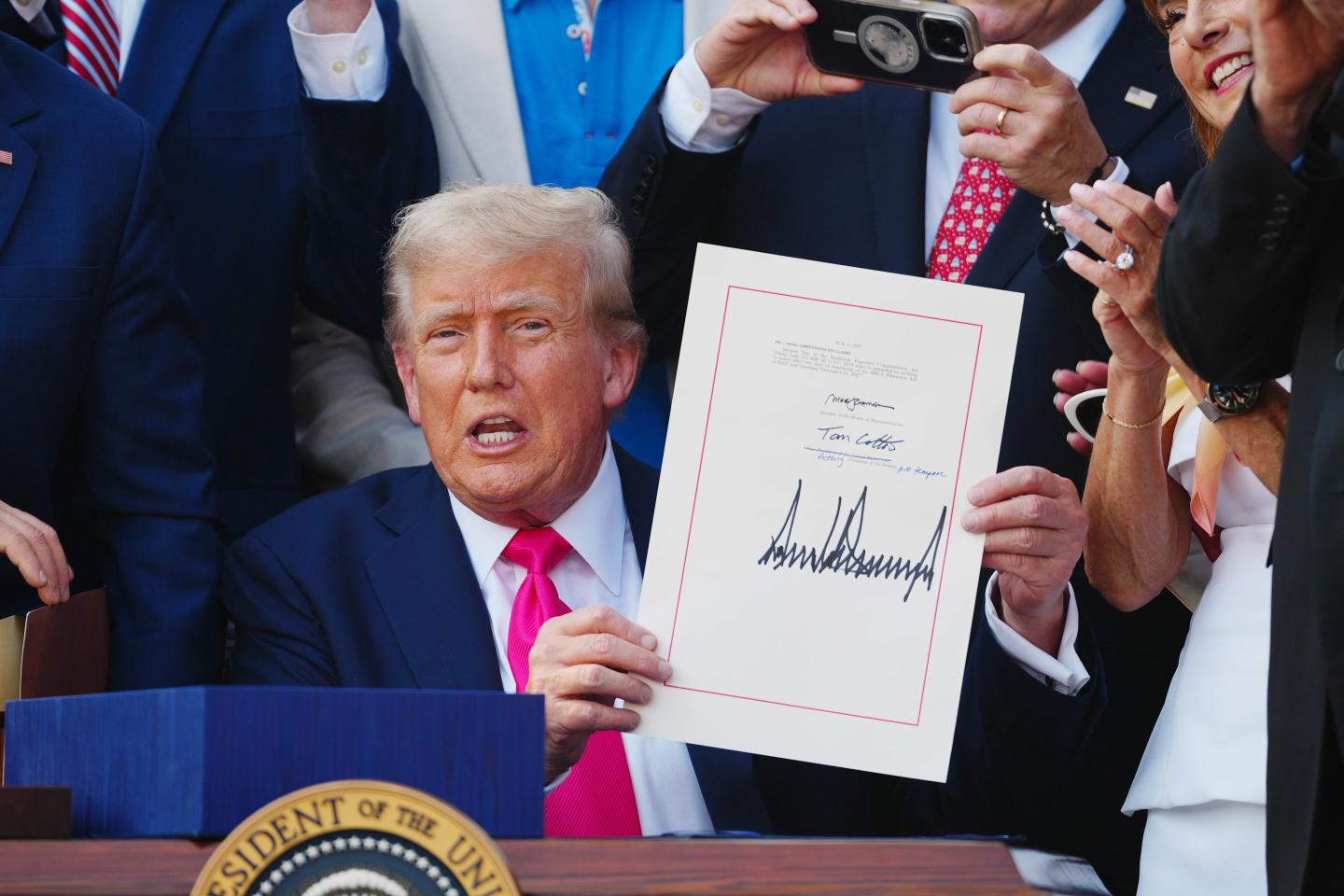Trump sits and shows a signed bill