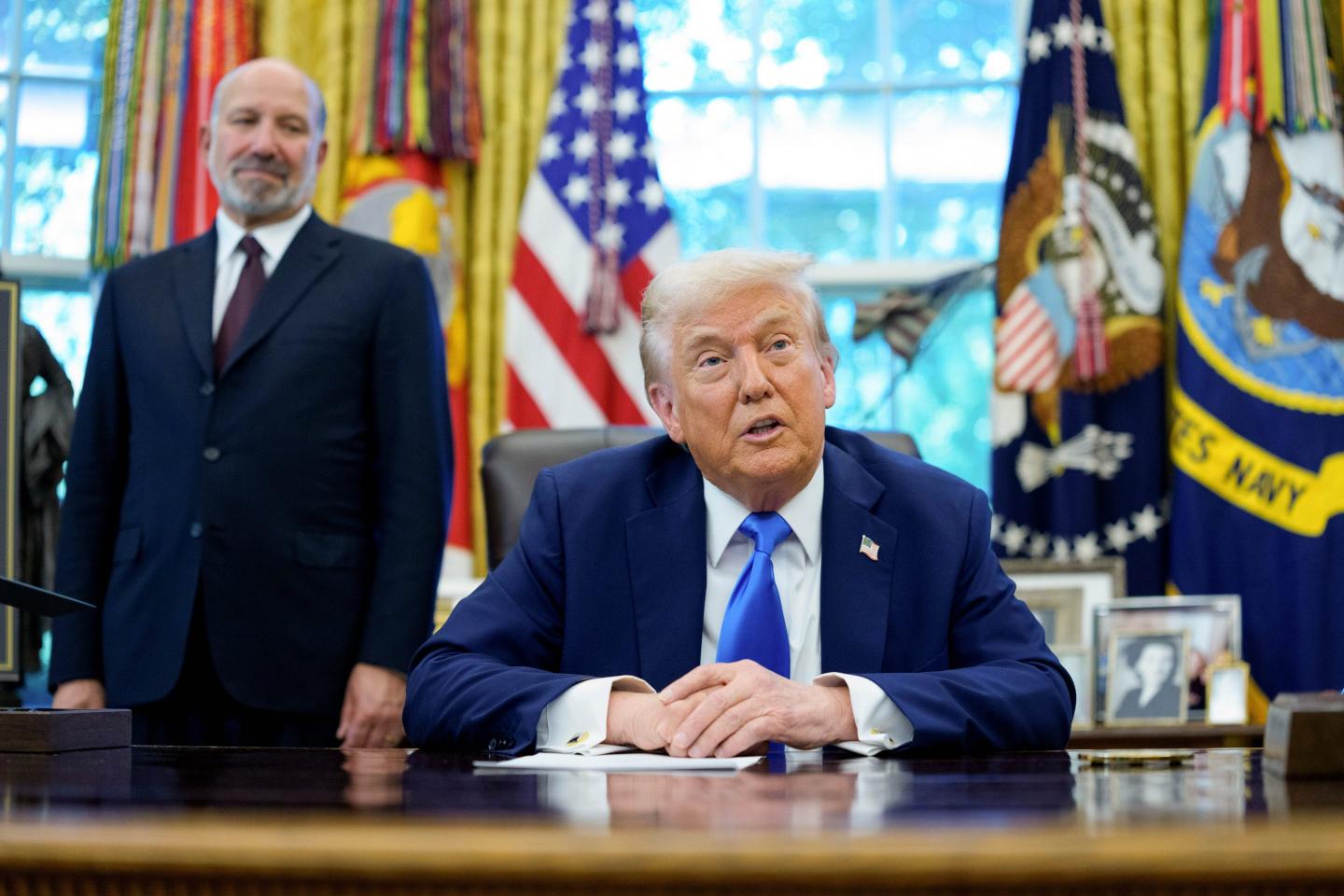 Trump sits at the Resolute Desk with his hands folded