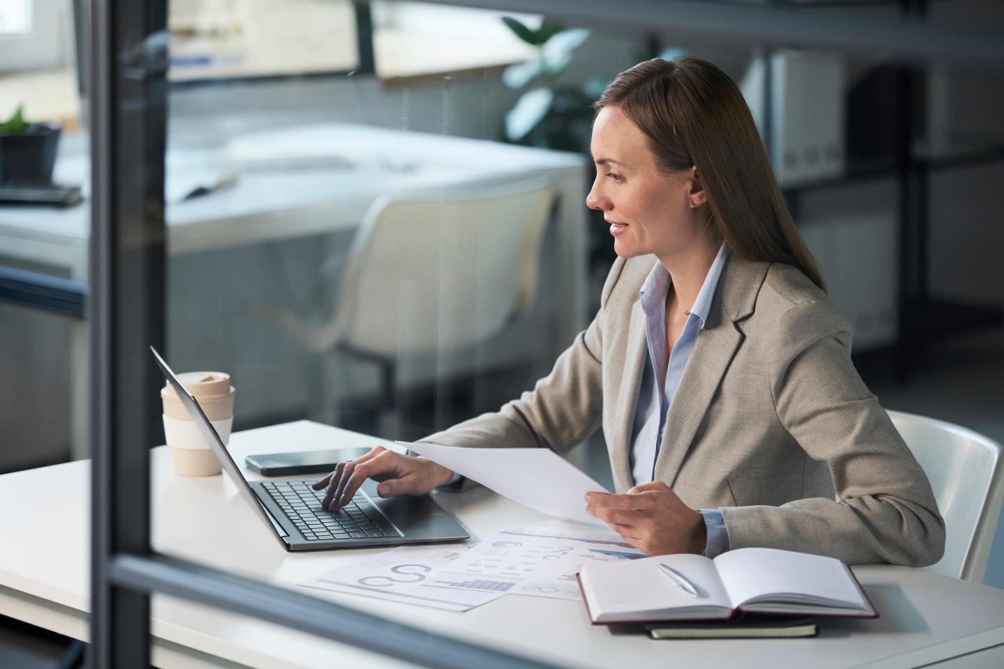 Businesswoman working at desk with laptop and documents in office