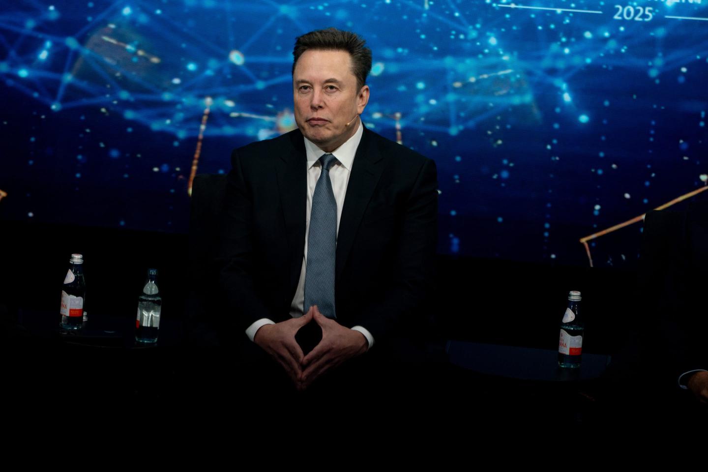 elon musk poses while wearing a suit