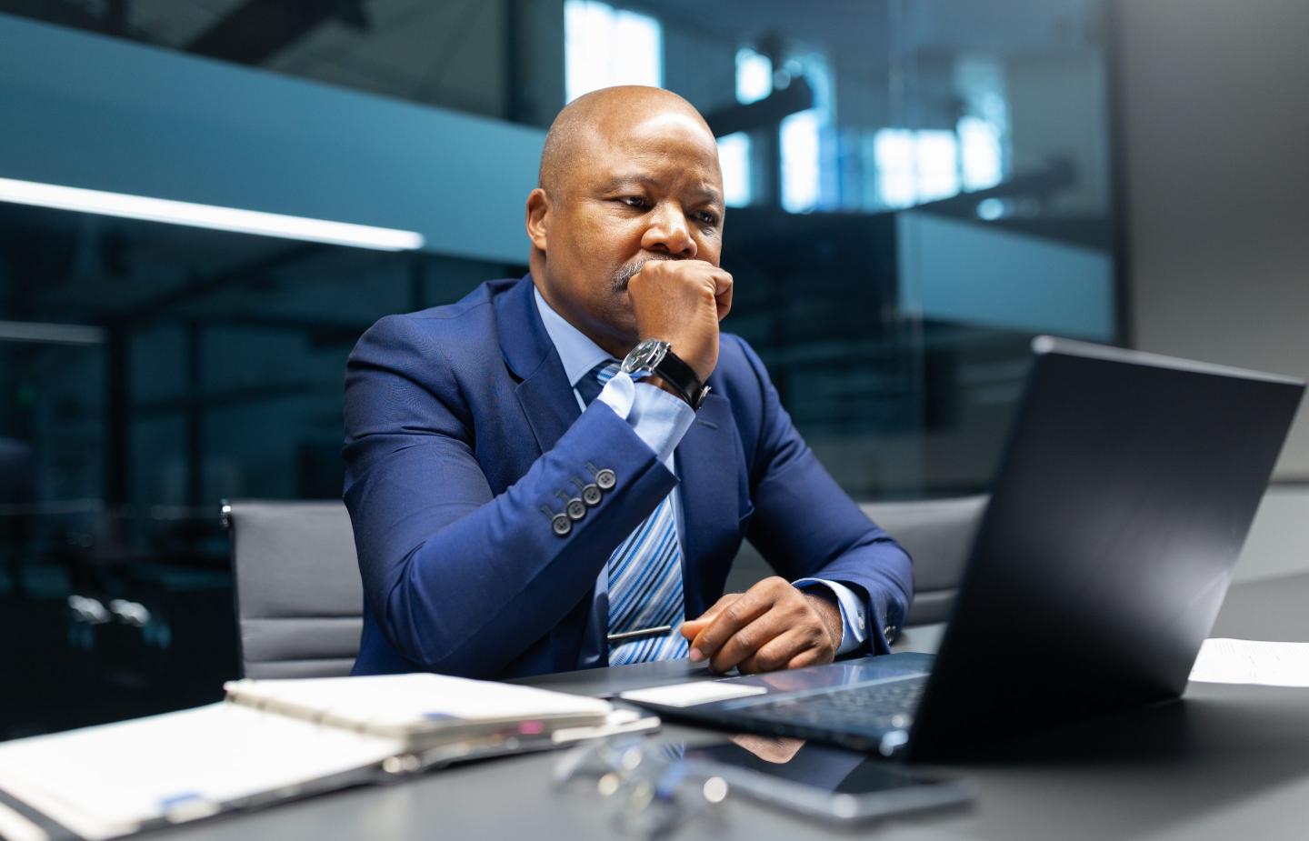 A man sits at desk and looks anxiously at a computer screen