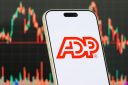 CHONGQING, CHINA - JANUARY 22: In this photo illustration, a smartphone displays the logo of Automatic Data Processing, Inc. (NASDAQ: ADP), an American provider of human capital management solutions including payroll, workforce management and business outsourcing services, in front of a screen showing the company's latest stock market chart on January 22, 2026, in Chongqing, China. (Photo illustration by Cheng Xin/Getty Images)