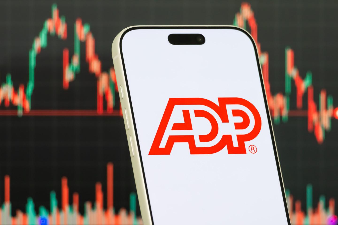CHONGQING, CHINA - JANUARY 22: In this photo illustration, a smartphone displays the logo of Automatic Data Processing, Inc. (NASDAQ: ADP), an American provider of human capital management solutions including payroll, workforce management and business outsourcing services, in front of a screen showing the company's latest stock market chart on January 22, 2026, in Chongqing, China. (Photo illustration by Cheng Xin/Getty Images)