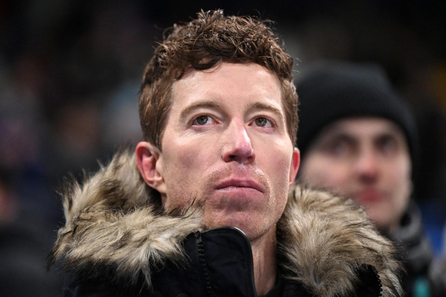 Shaun White, wearing a jacket with a fur-lined hood, looks up.