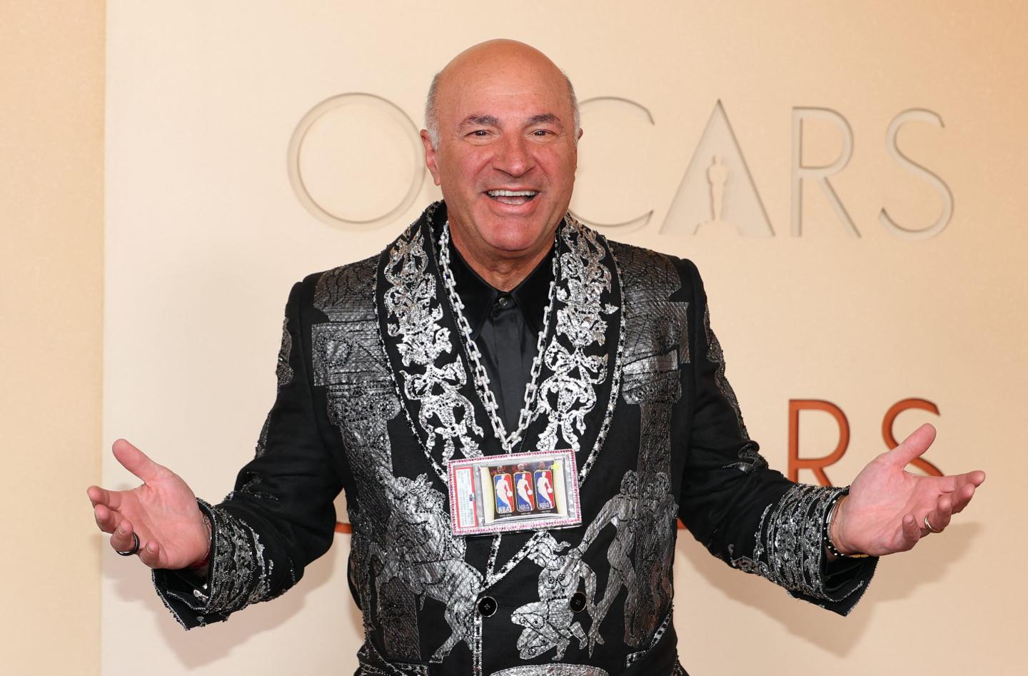 Kevin O'Leary wears a silver and black suit with a chain of basketball cards around his neck.