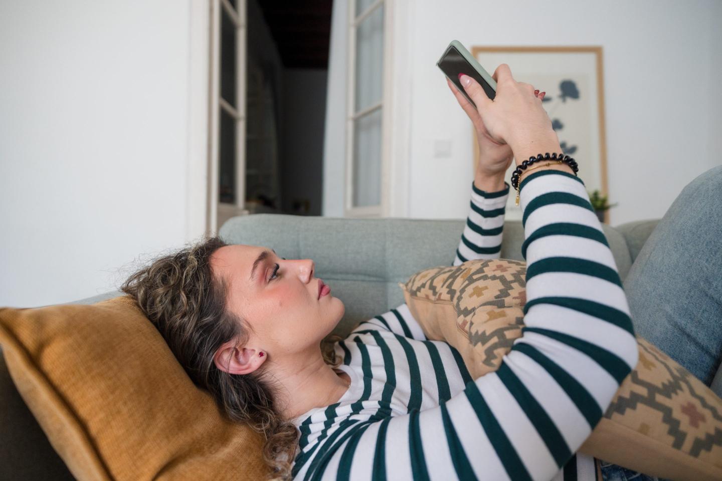 Young woman relaxing on sofa at home, scrolling smartphone