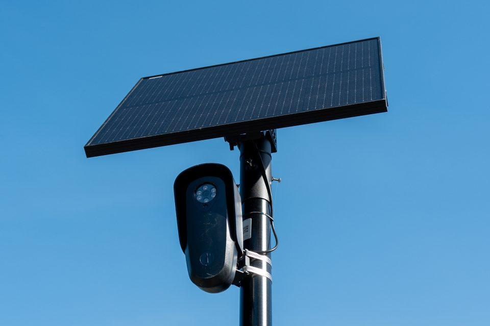 A Flock camera attached to a solar panel against a blue sky.