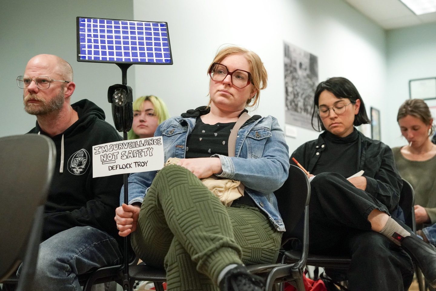 A person holding a protest sign sits with their legs crossed.