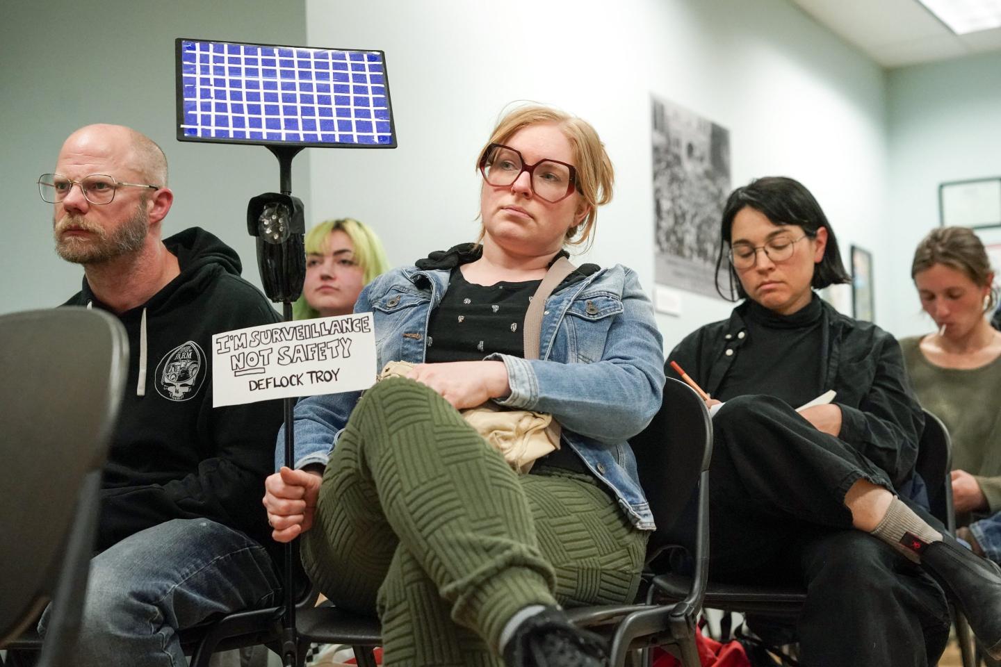 A person holding a protest sign sits with their legs crossed.
