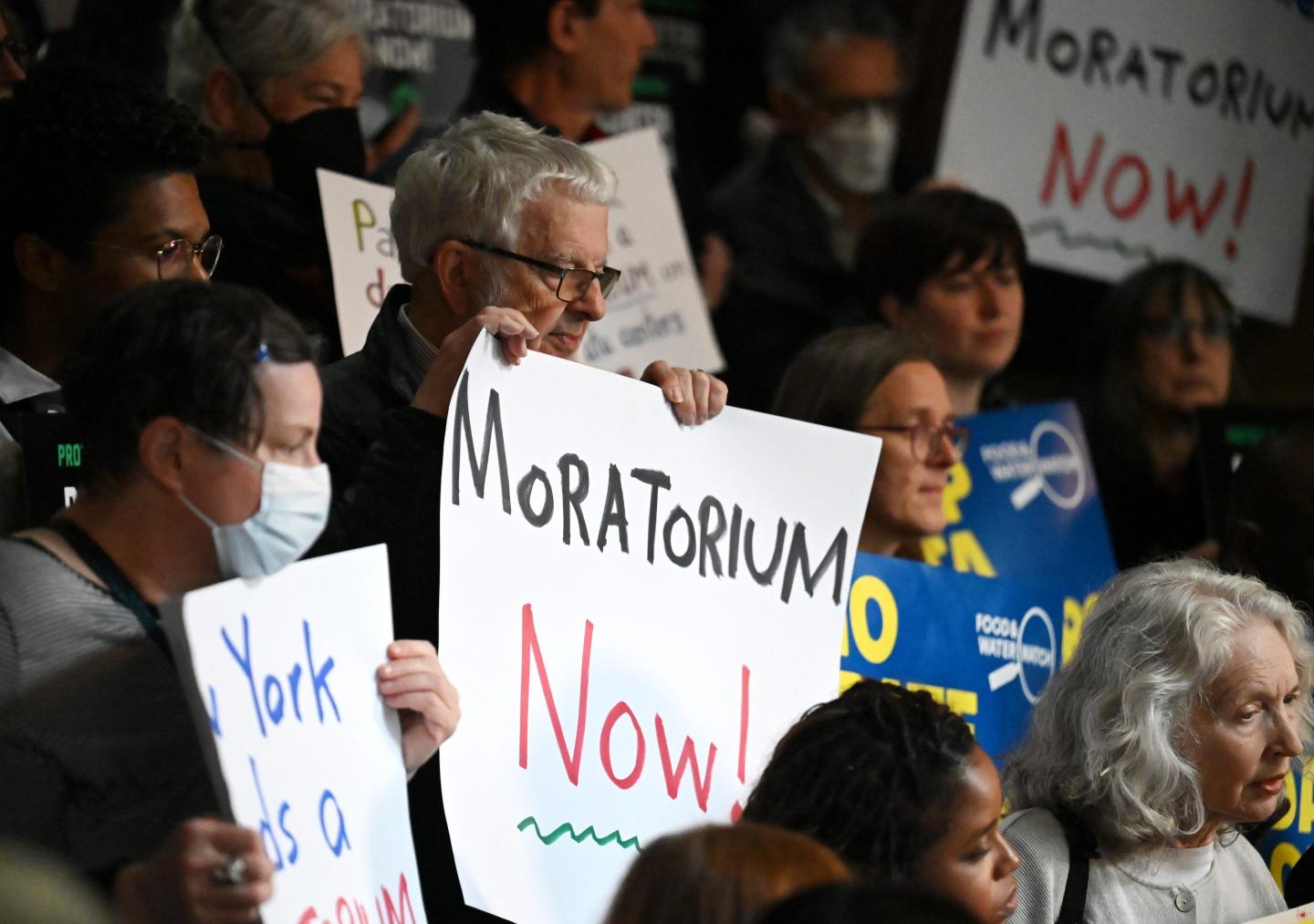 A man in a crowd holds a sign that says, "Moratorium NOW!"