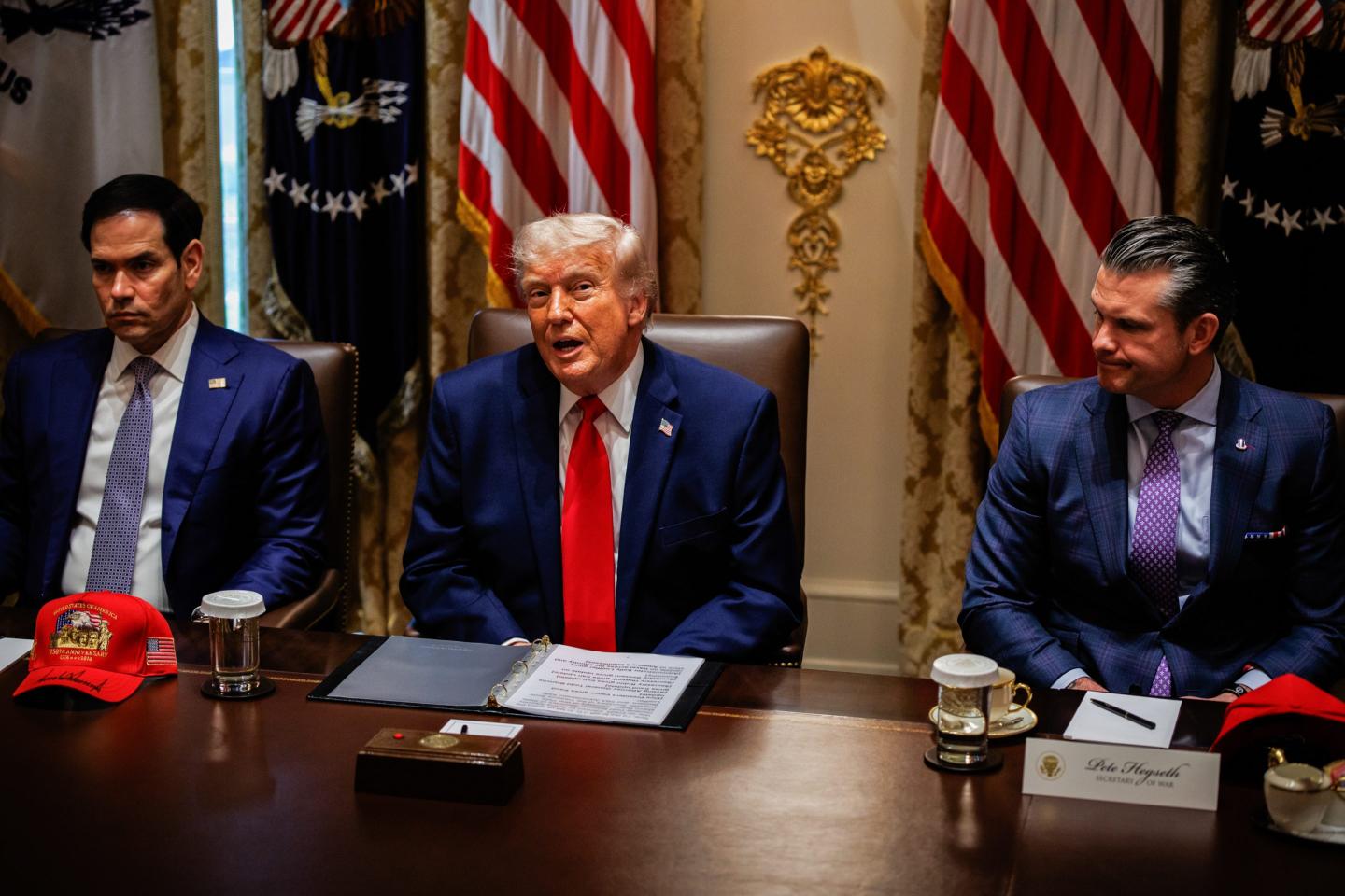 Trump, Rubio, and Hegseth sit next to each other at a dark wooden table.