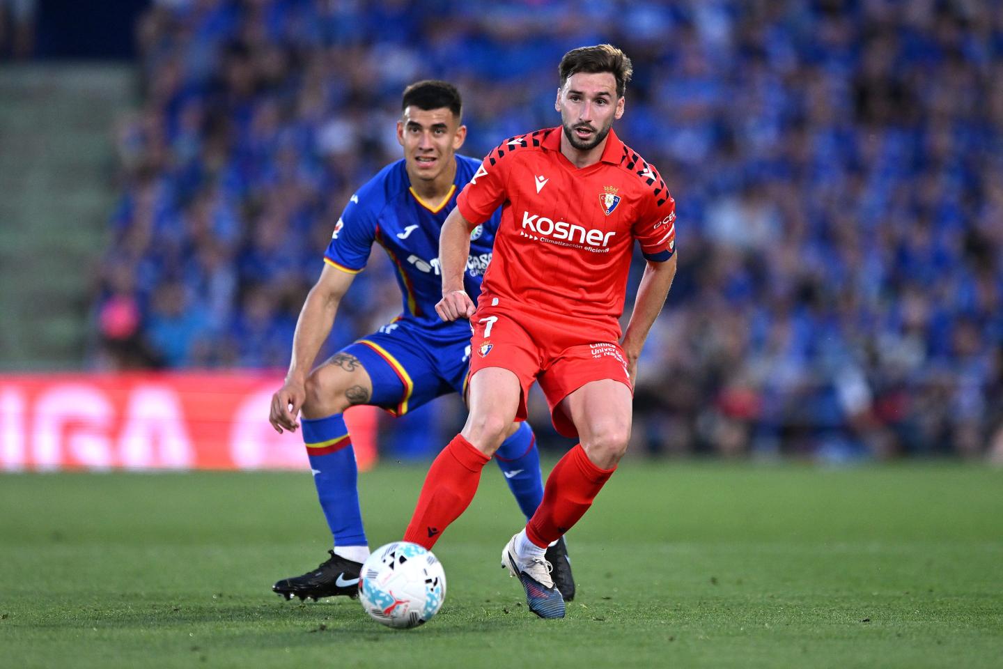 An Osasuna player passes the ball while under pressure from Getafe rival.