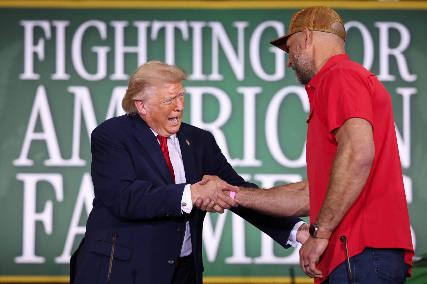 Donald Trump shakes the hand of a farmer wearing a red shirt