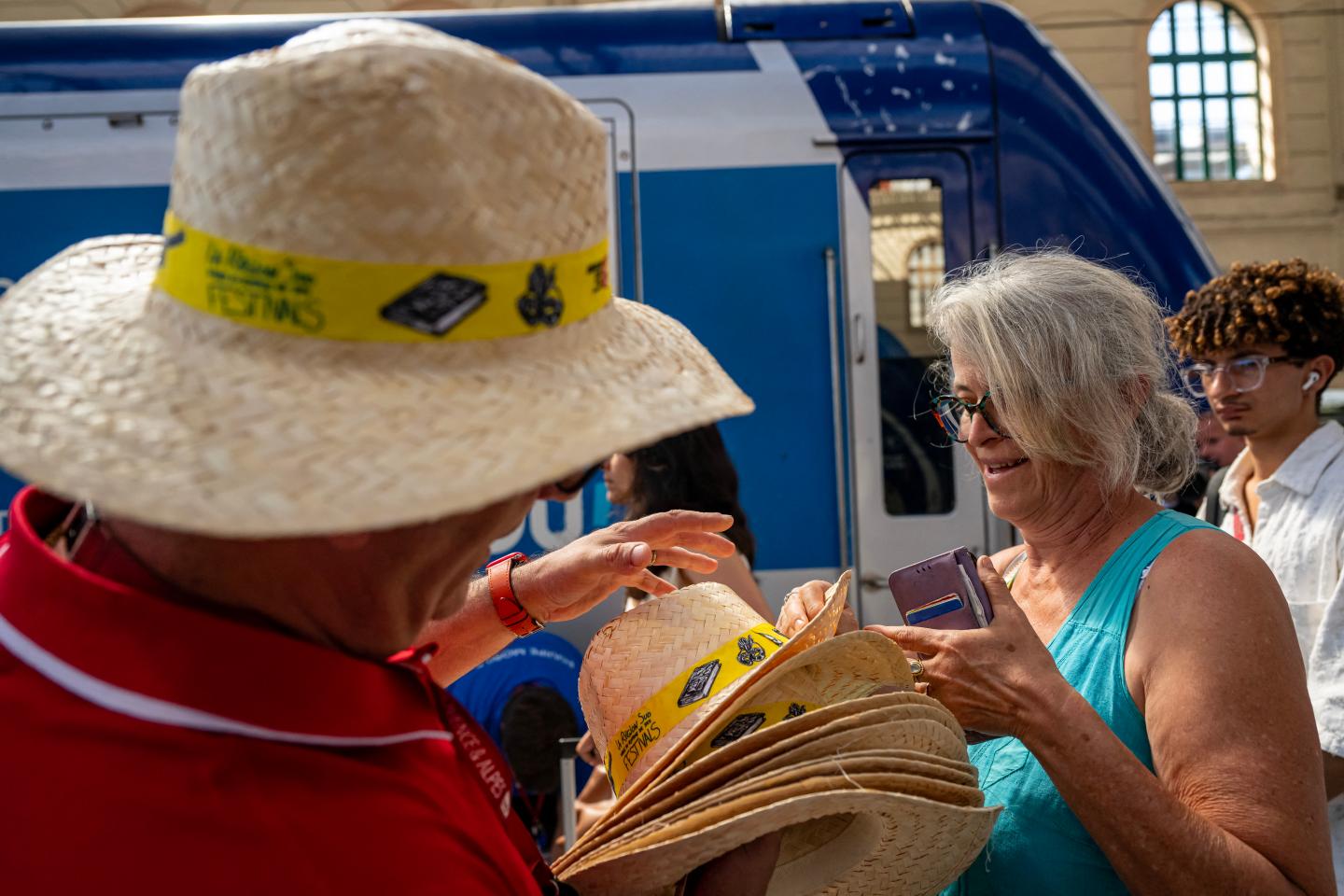 A man watching a straw hat hands a woman with gray hair a hat.
