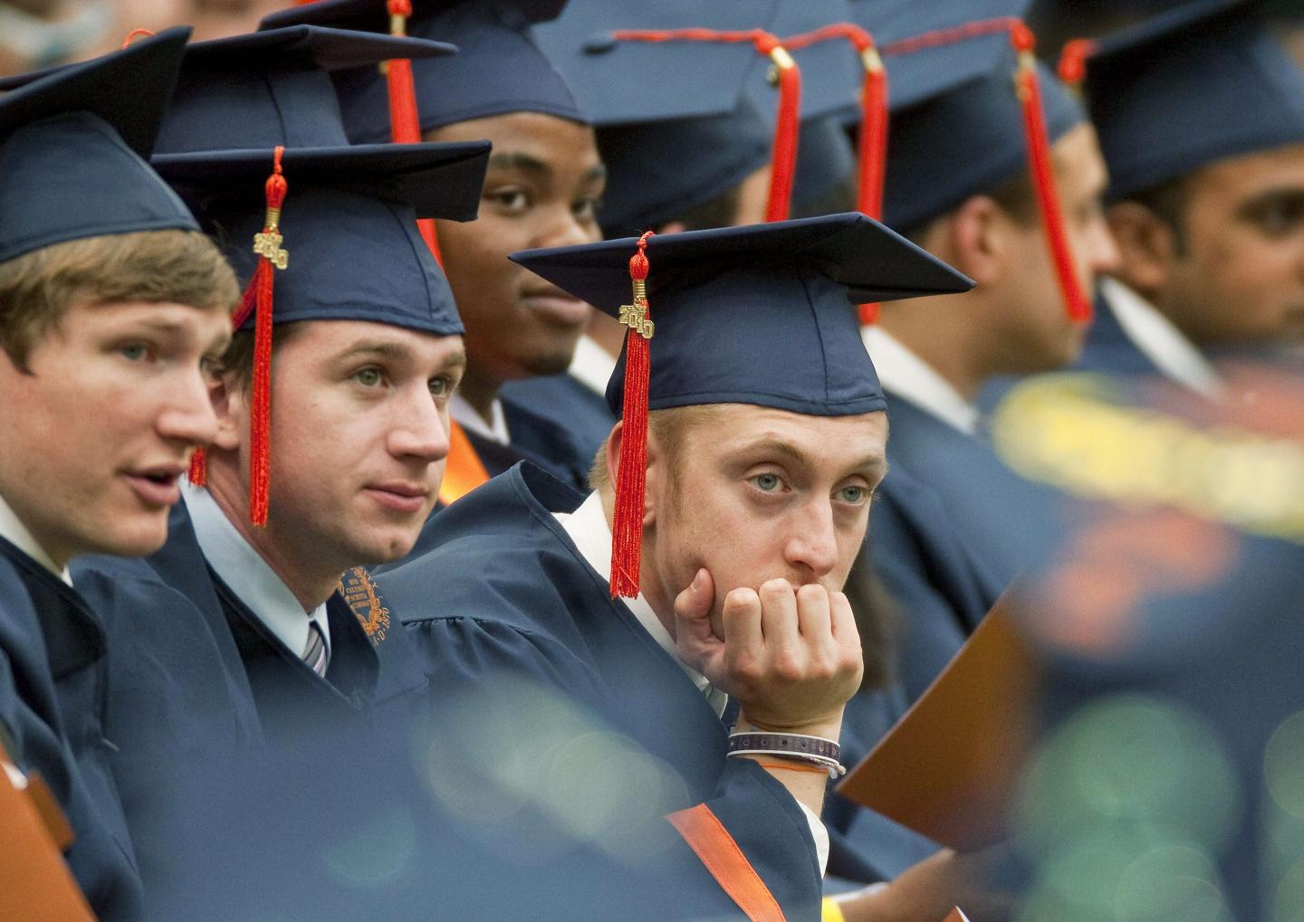 A college graduate in regalia rests his chin in his hand.