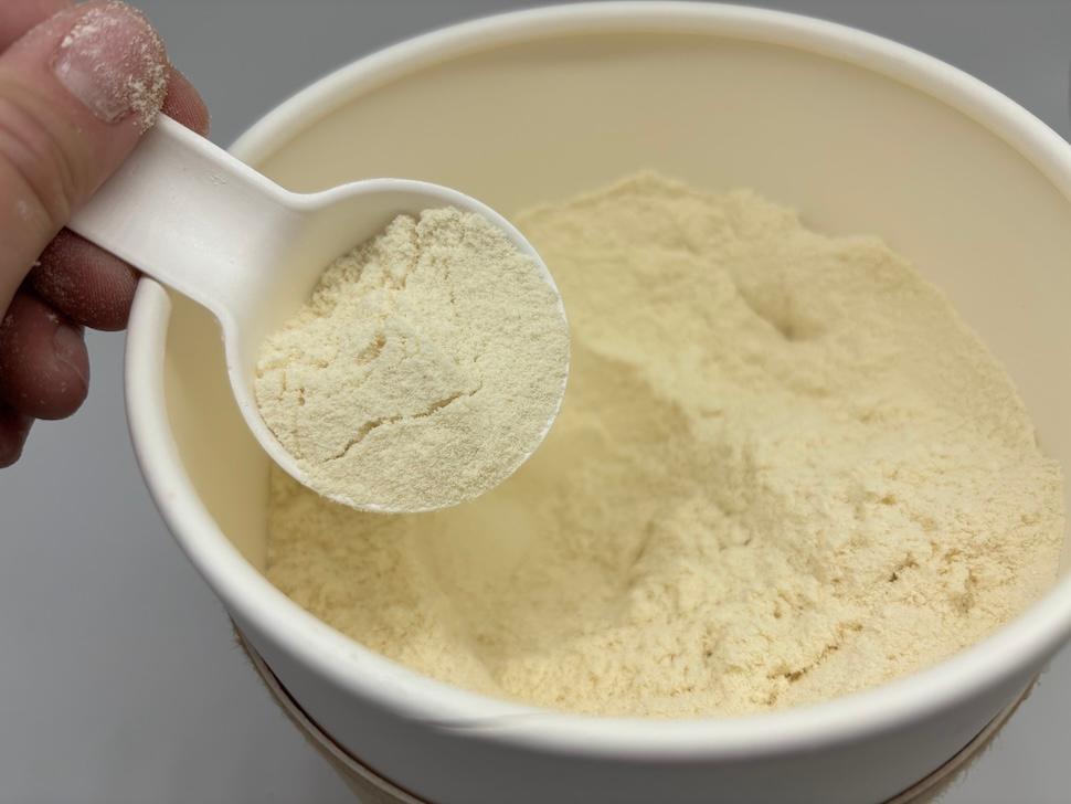 An open canister of Heart & Soil Animal-Base Protein. A hand is scooping out some of the off-white powder.