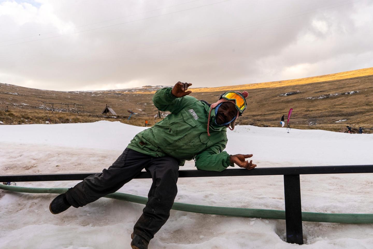 A ski worker in winter skiing gear strikes a pose in front of a ski slope in Lesotho.