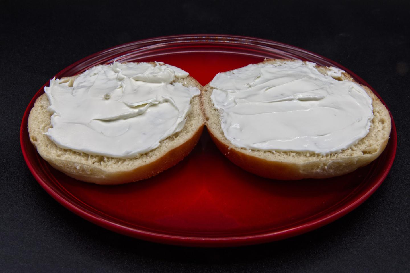 An open plain bagel with cream cheese smeared on a plate.