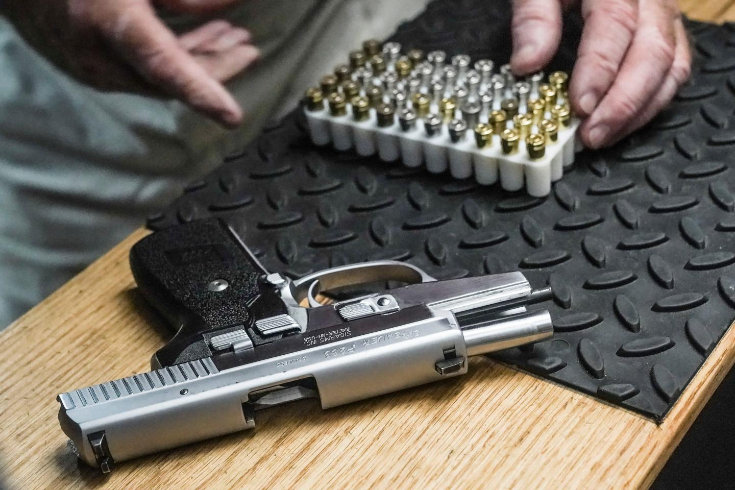 A gun lays on a table next to a row of ammunition.