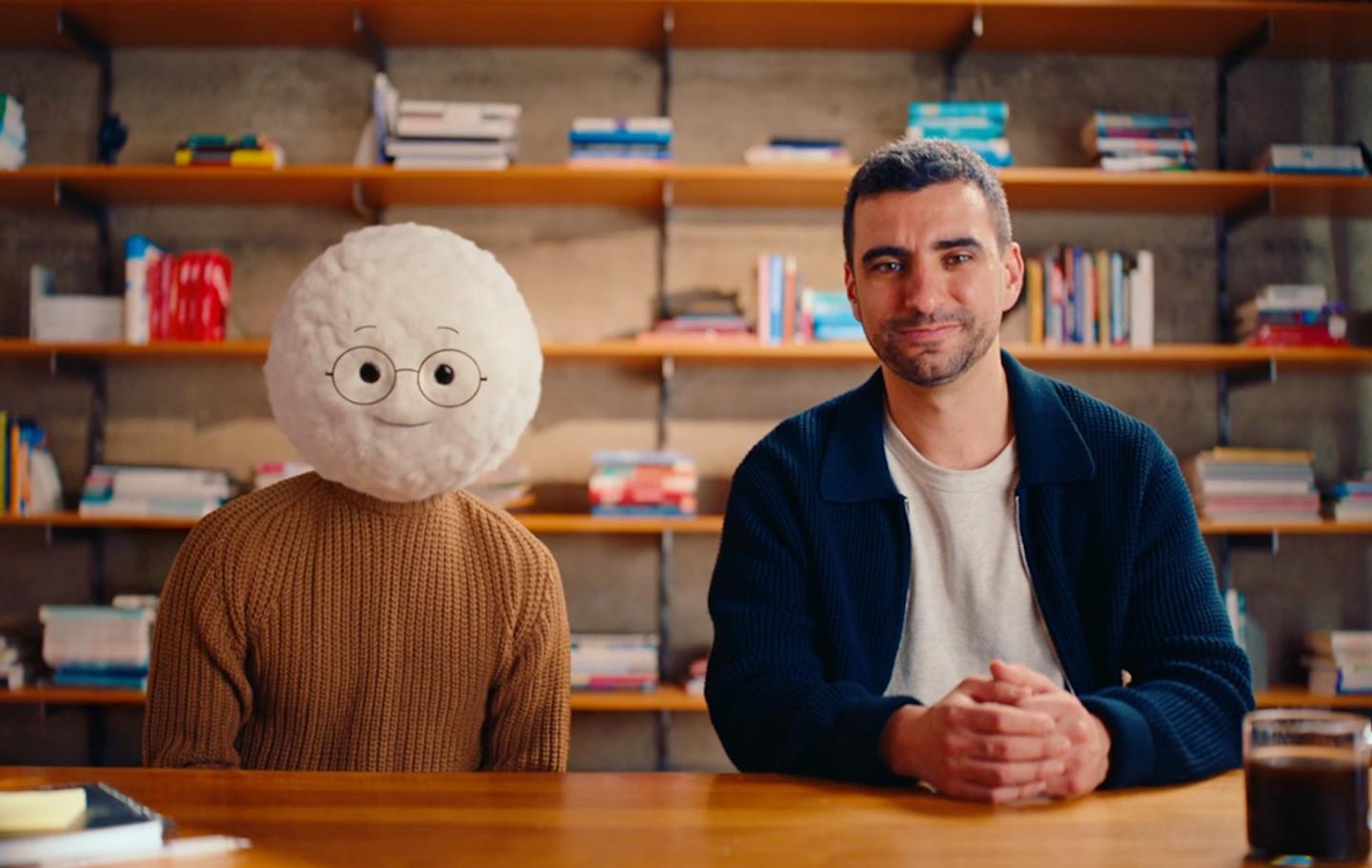 Aiden, an AI bot cartoon, poses next to Nim Ravid.