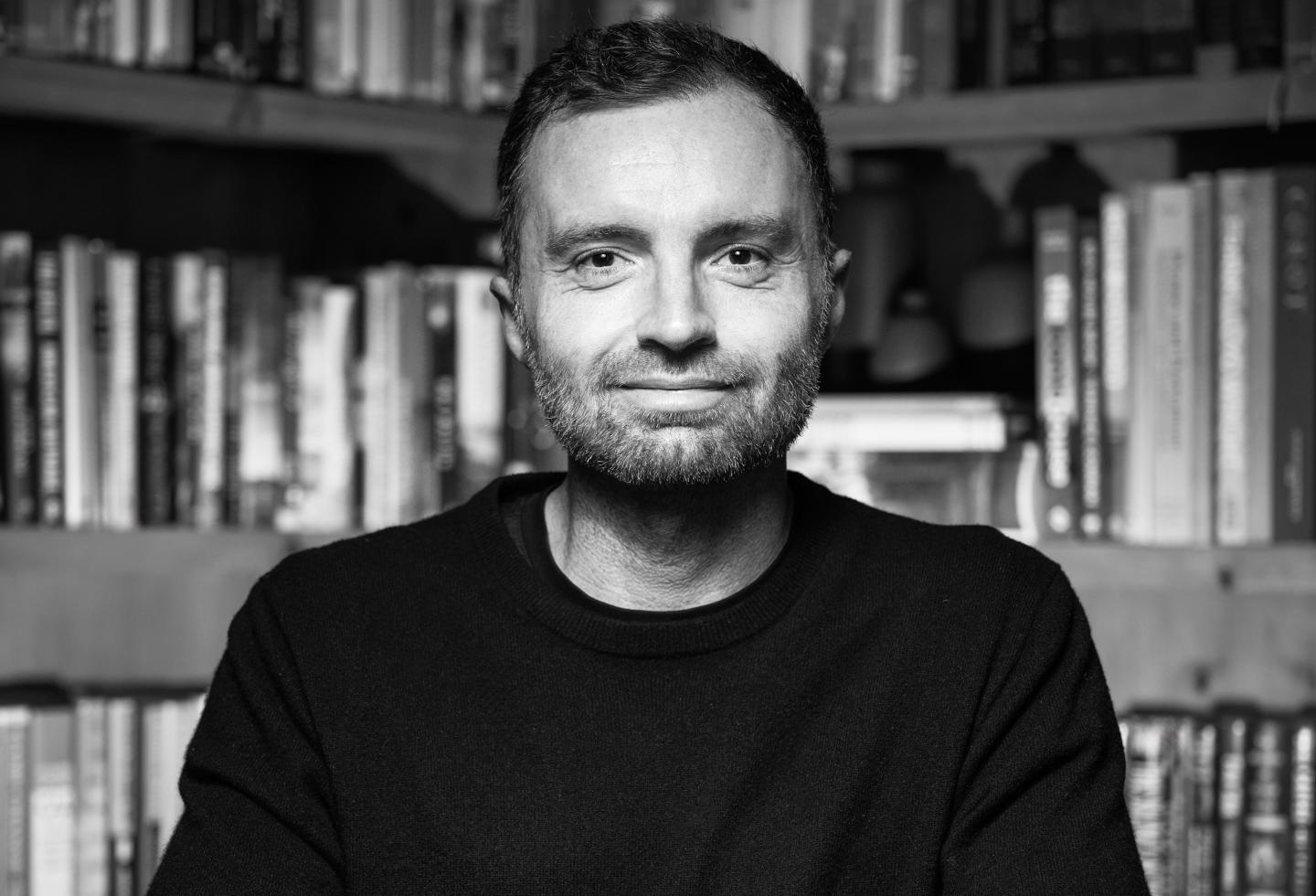 David Senra poses in a black shirt in front of bookshelves