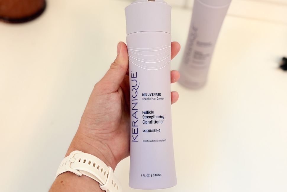 Closeup of a hand holding a bottle of Keranique Follicle Strengthening Conditioner.