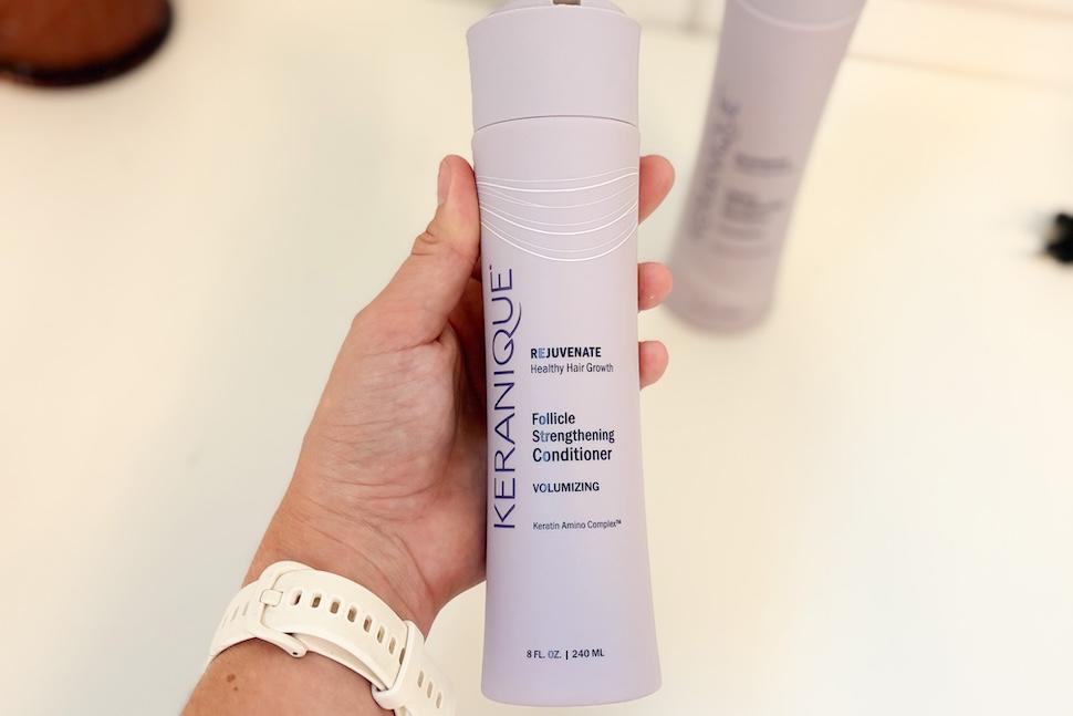 Closeup of a hand holding a bottle of Keranique Follicle Strengthening Conditioner.