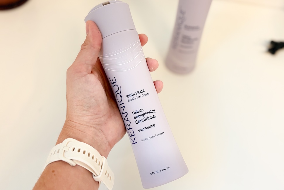 Closeup of a hand holding a bottle of Keranique Follicle Strengthening Conditioner.