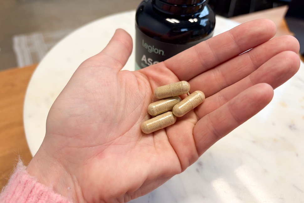 An open palm holding four Legion Ascend capsules. The capsules have a goldish hue.