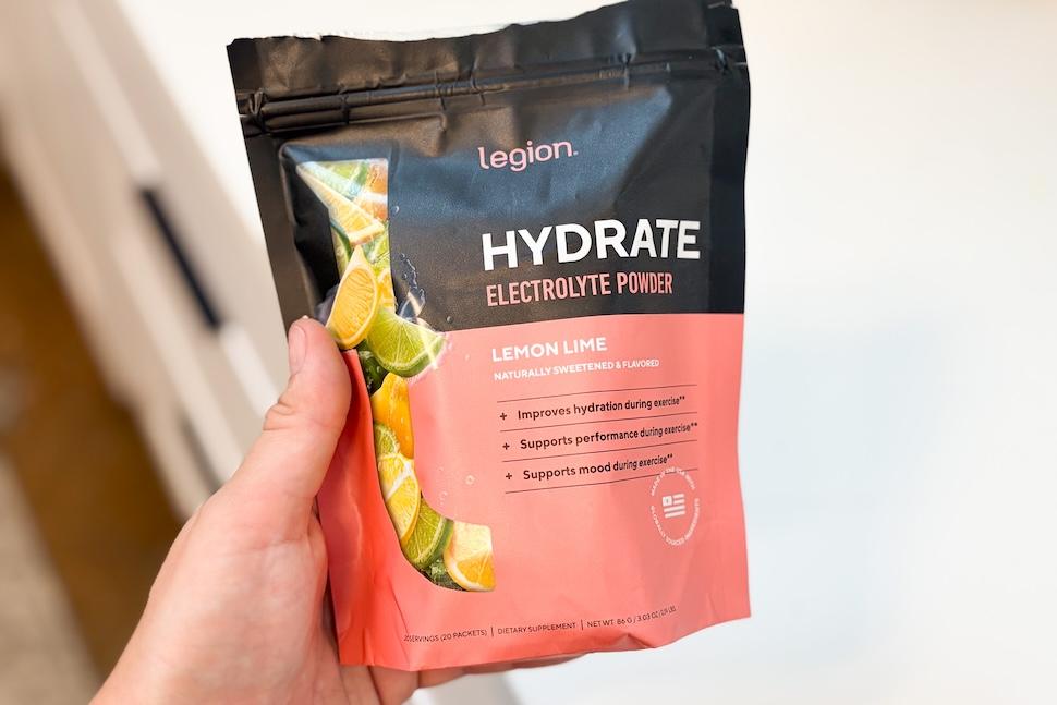 A hand holding a bag of Legion Hydrate electrolyte powder (lemon lime flavor)