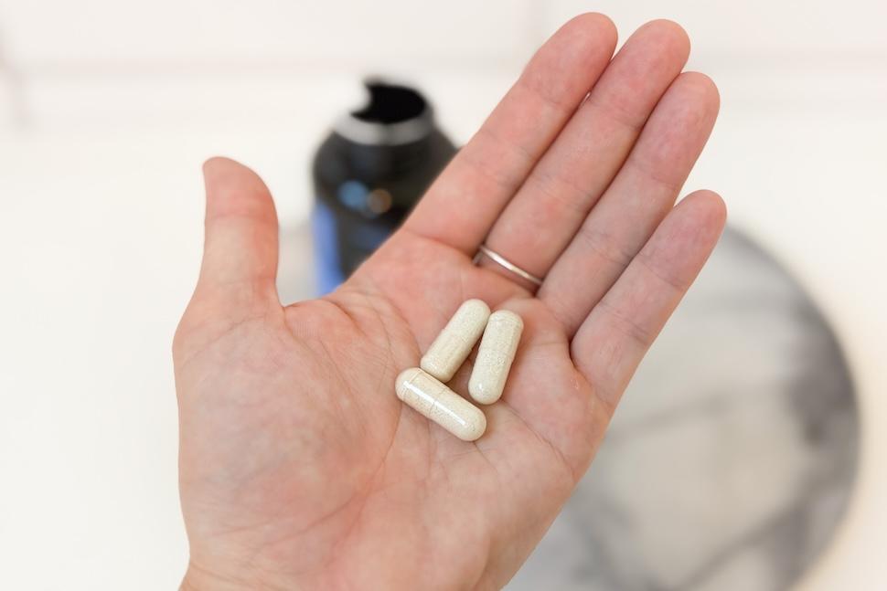 An open palm holding three off-white capsules of Legion Triumph Prenatal Vitamins