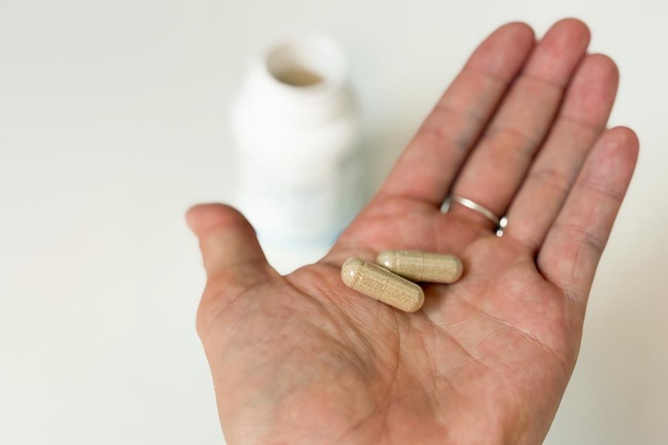Closeup of an open palm holding two Mind Lab Pro v4 capsules. The capsules have a goldish hue, and you can see the open bottle on the countertop below.