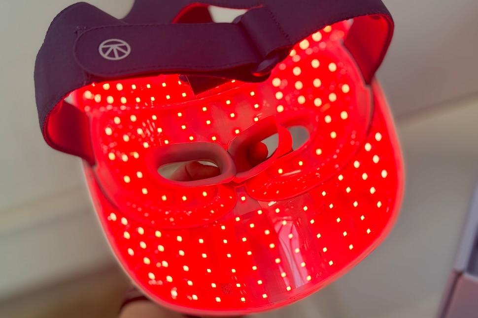The Therabody TheraFace Mask Glo lying face down. It's lit up and you can see the red light inside it.