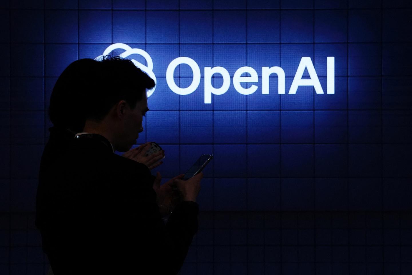 Visitor look at their phone next to an Open AI's logo during the Mobile World Congress (MWC), the telecom industry's biggest annual gathering, in Barcelona on February 26, 2024. The world's biggest mobile phone fair throws open its doors in Barcelona with the sector looking to artificial intelligence to try and reverse declining sales. (Photo by PAU BARRENA / AFP) (Photo by PAU BARRENA/AFP via Getty Images)